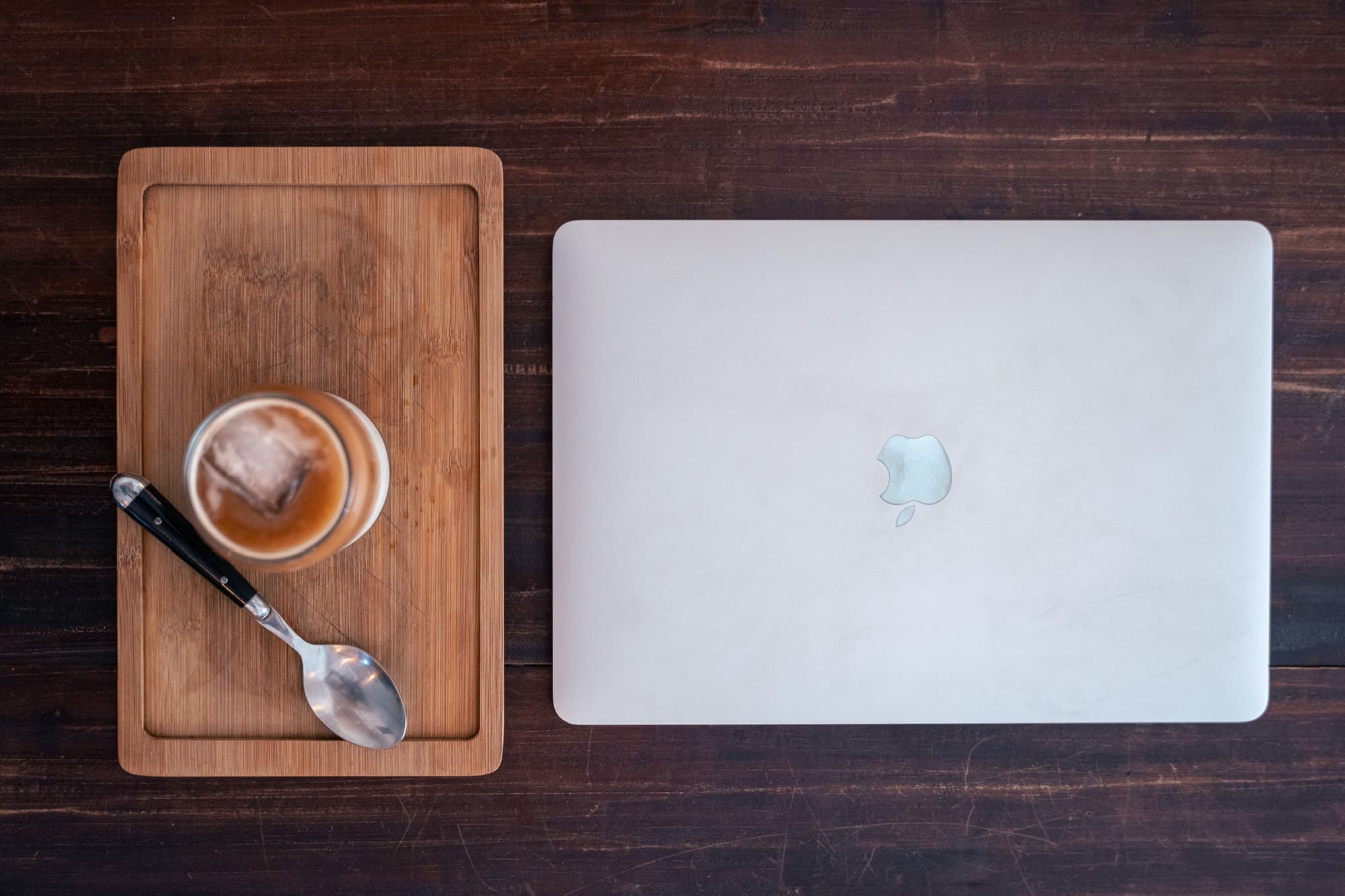 Un vaso de café sobre una tabla de madera, junto a un portátil cerrado.