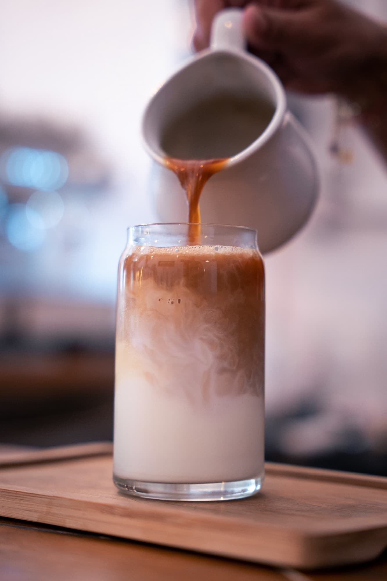 Café vertido desde una jarrita en un vaso de leche con hielo.