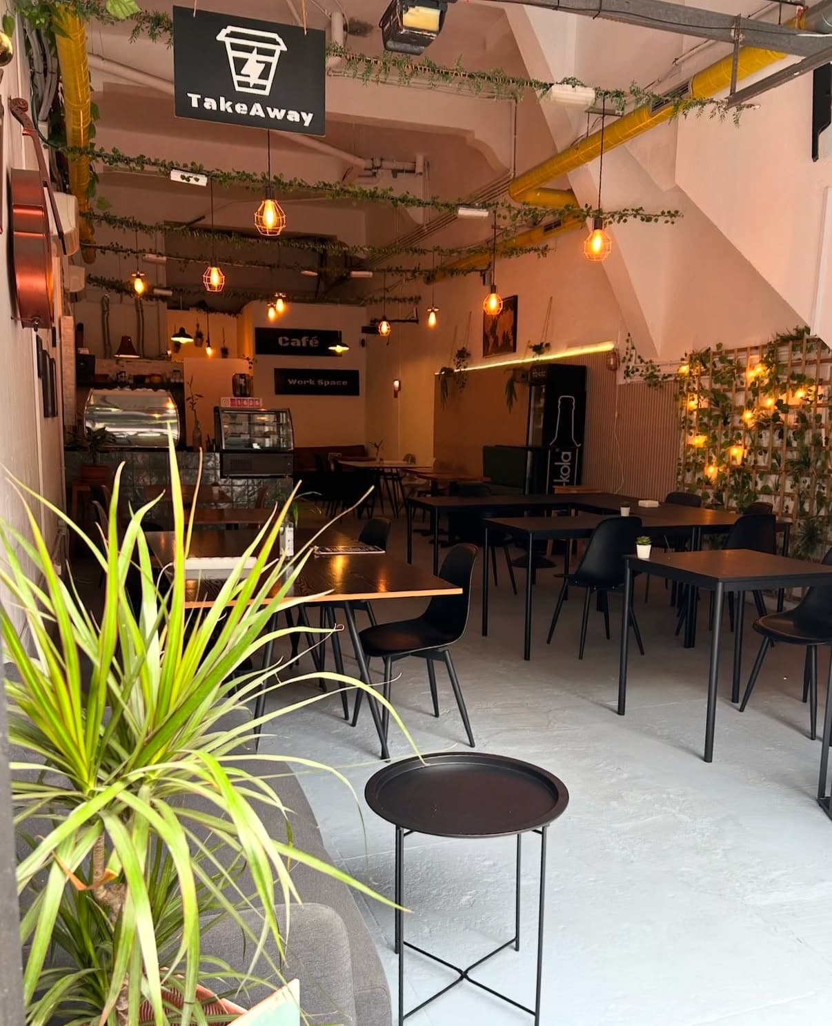 Im Café: Pflanzen, hängende Glühbirnen und gedeckte Tische.
