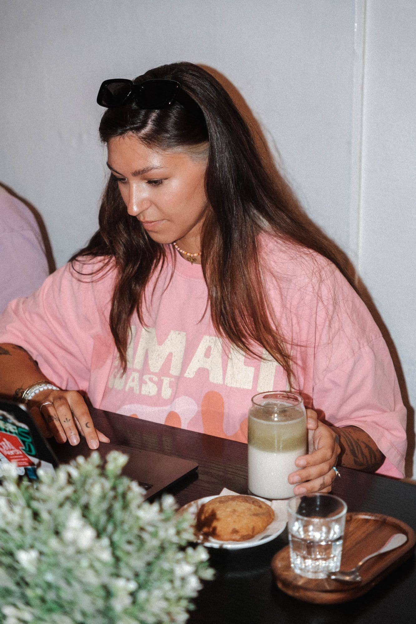 Una chica con un matcha latte con hielo y una galleta, junto a su portátil.