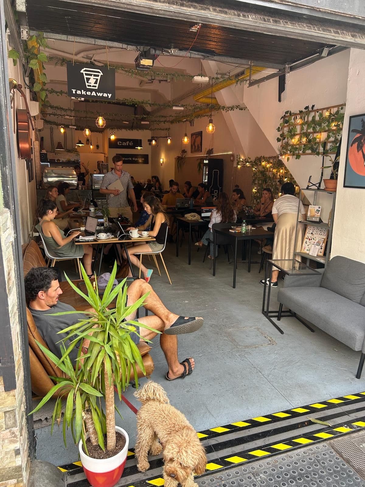 El café visto desde la puerta: gente trabajando en las mesas, un chico en el sofá de cuero y un perro en la entrada.
