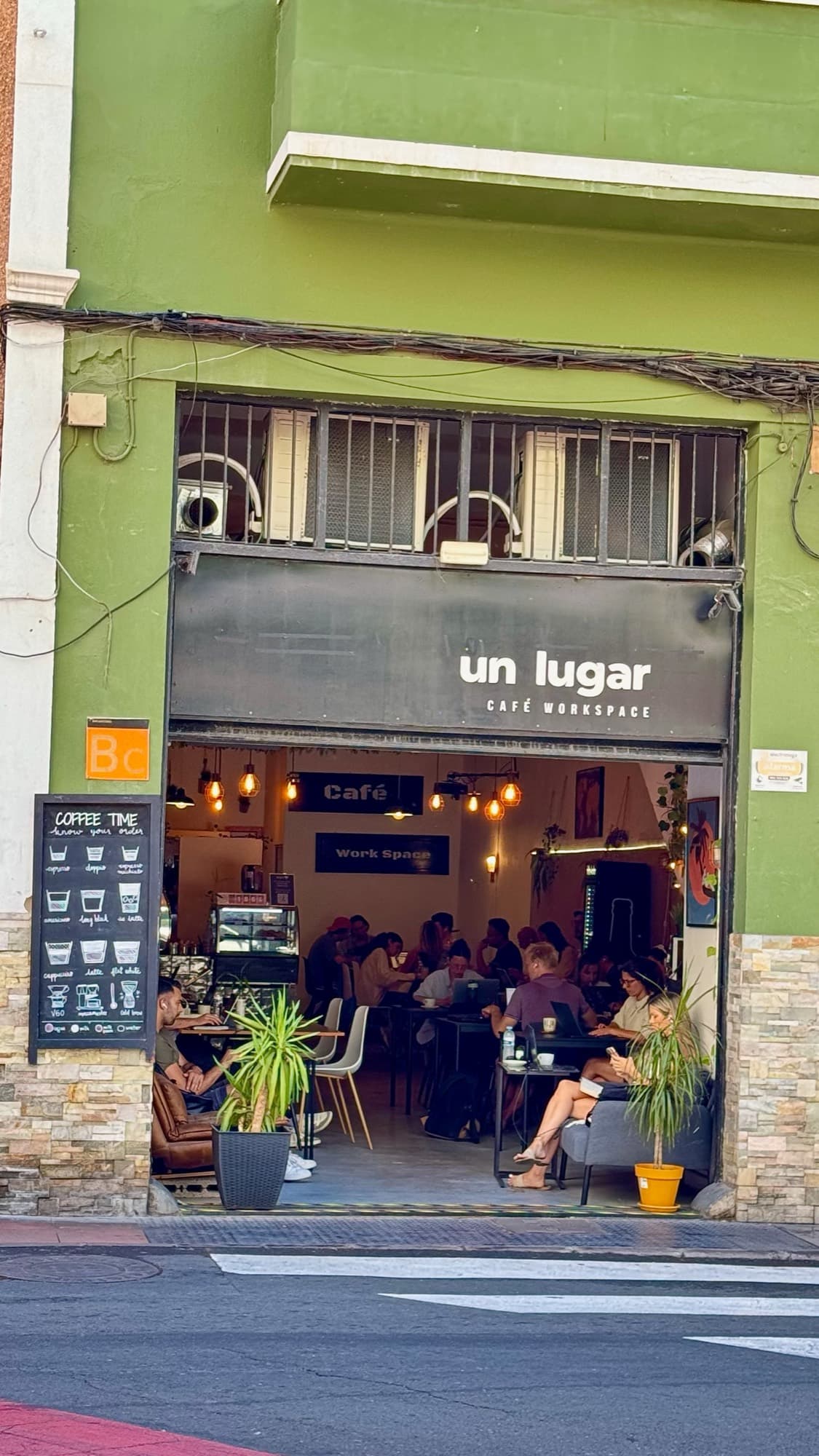 La fachada verde de Un Lugar Café Workspace desde la calle, con el local lleno de gente.