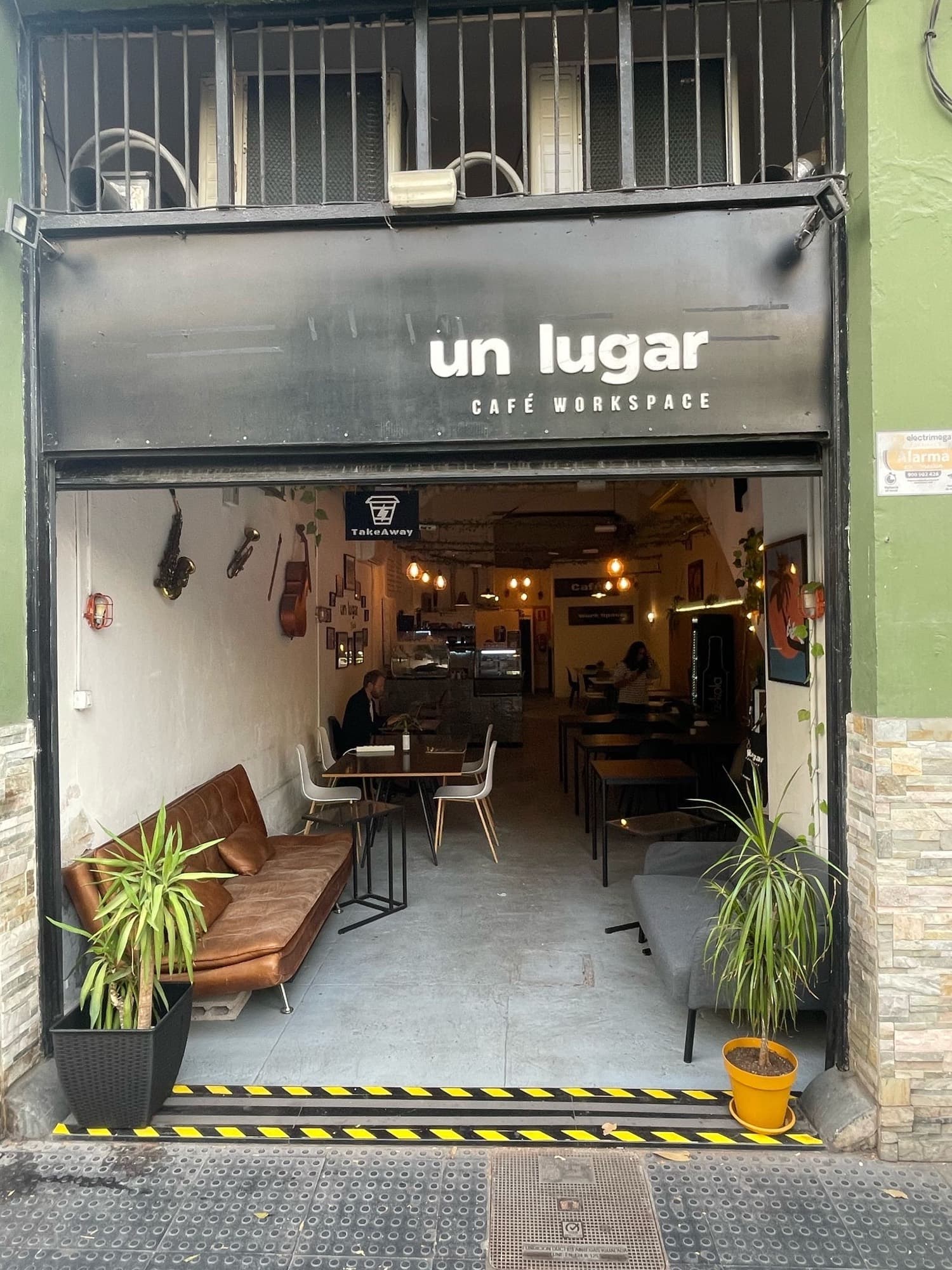 La entrada de Un Lugar Café Workspace con la persiana subida, sofás y plantas en la puerta.