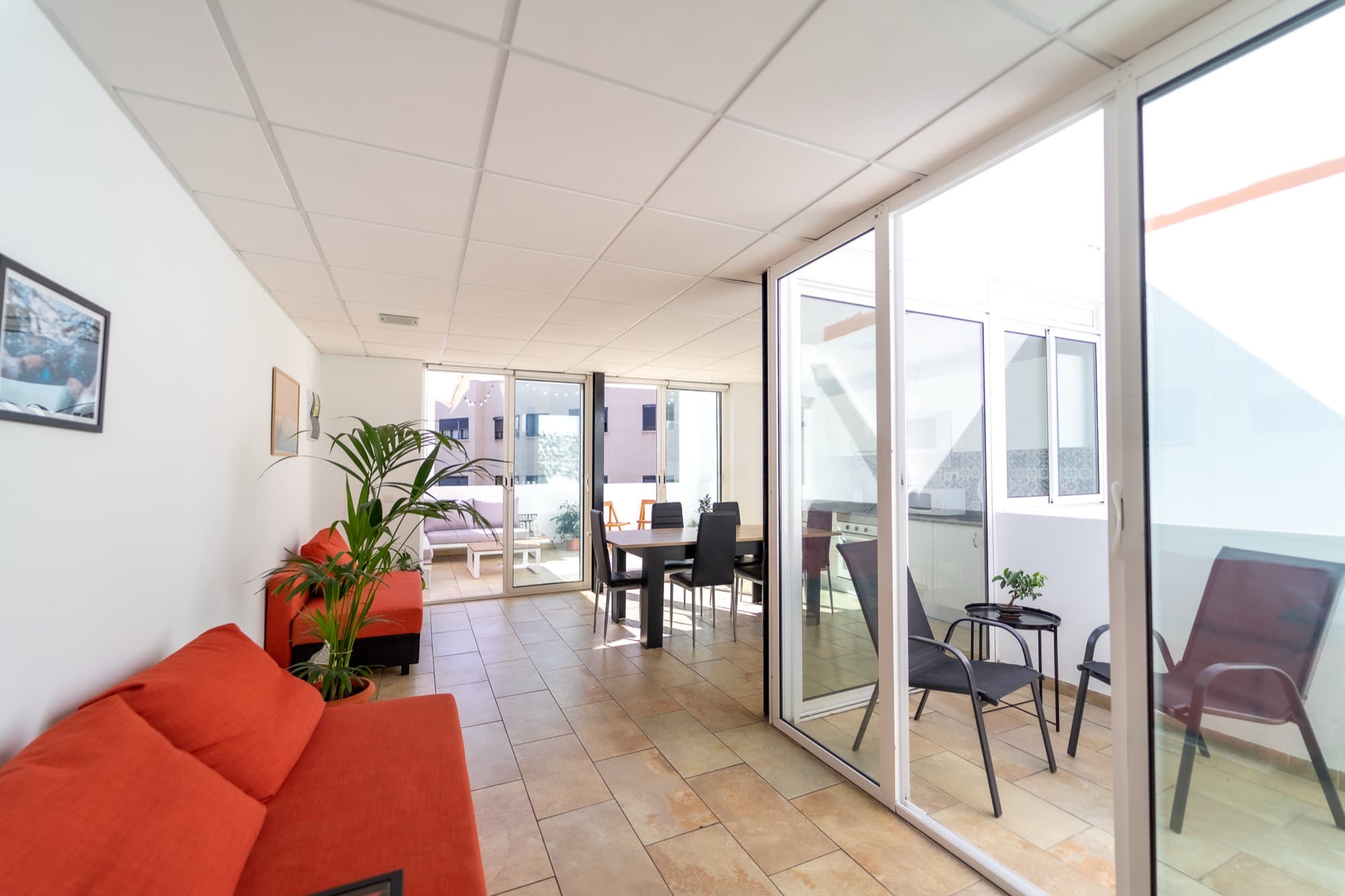 Salón común con sofá rojo, mesa de comedor y puertas de cristal que dan a la terraza.