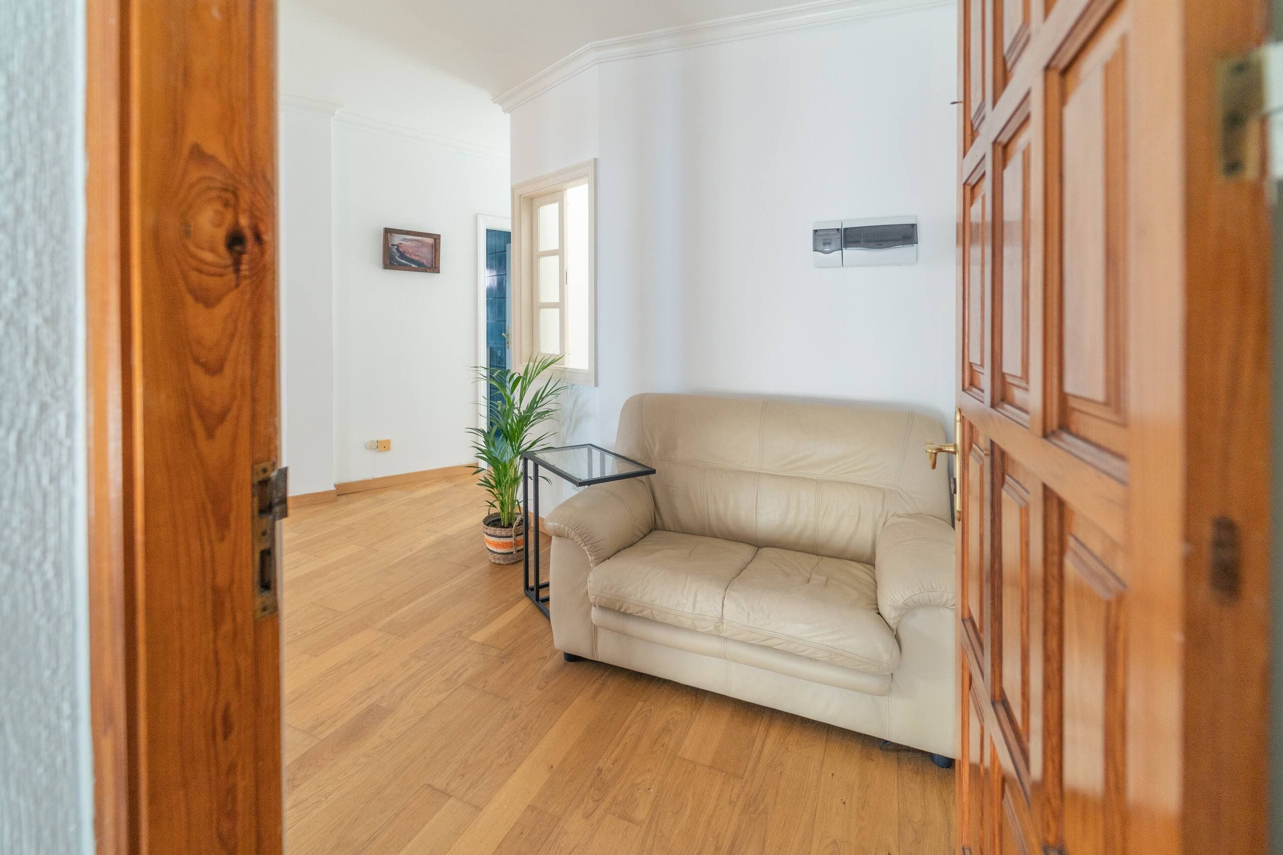 Rincón del salón con sillón crema, planta y suelo de madera.