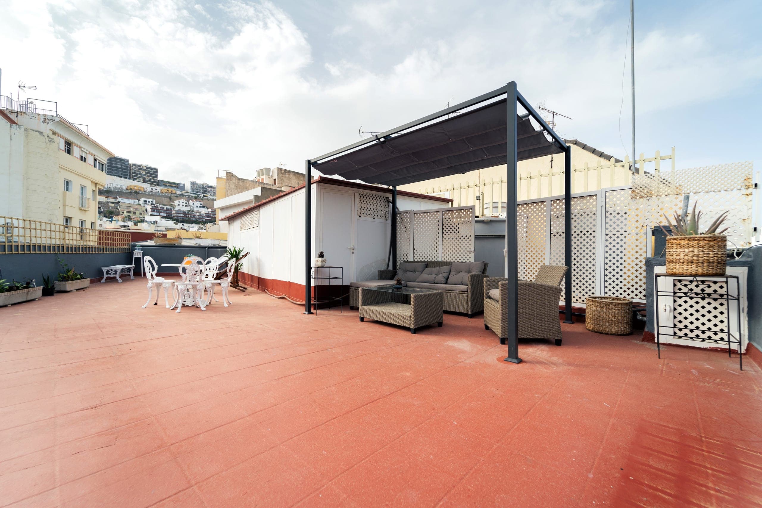 La gran terraza de House San Telmo: pérgola con sofás exteriores, mesa y sillas, y vistas a los tejados de la ciudad.