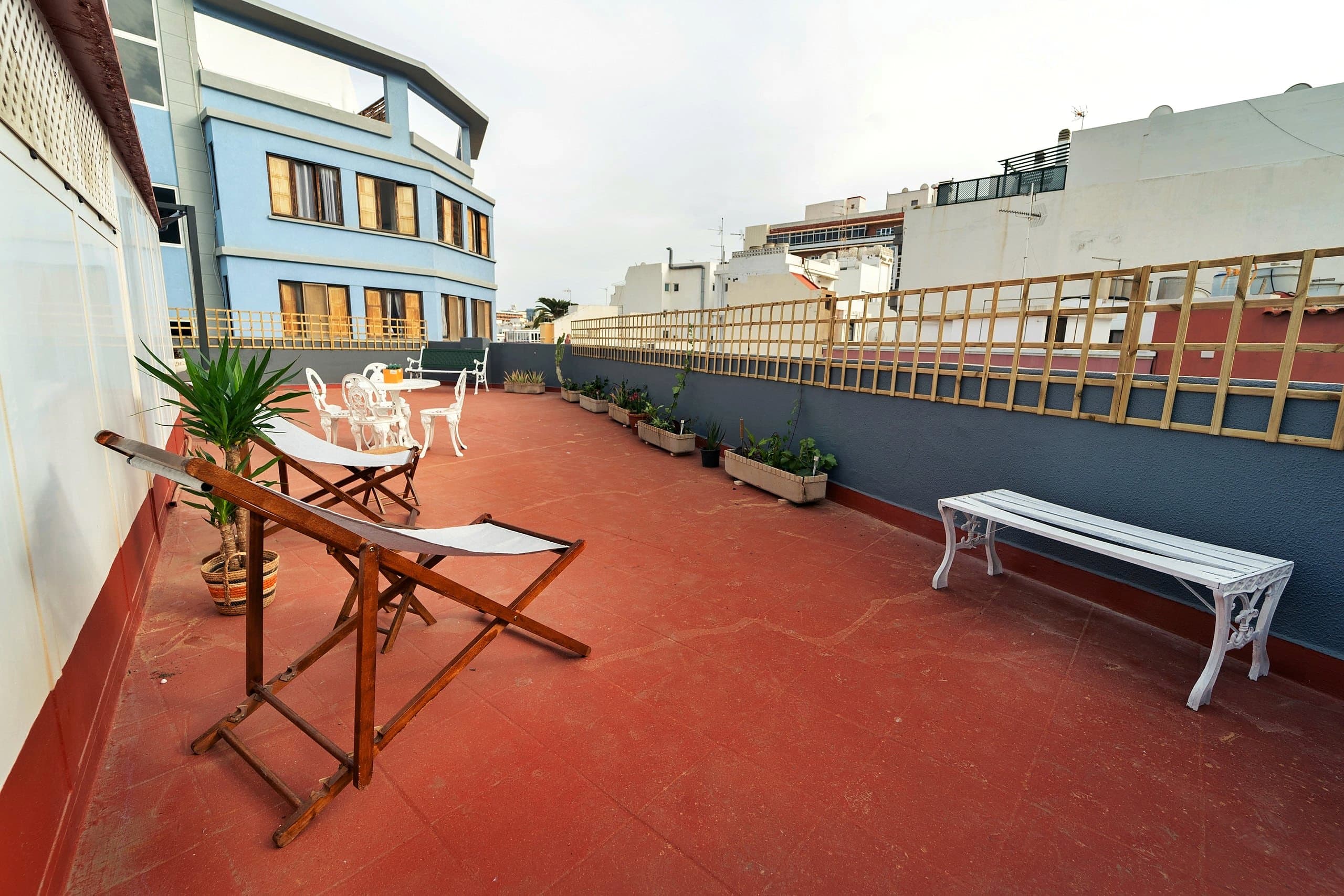 La azotea de House San Telmo: dos tumbonas de madera con lona gris, una yuca en maceta, mesa y sillas blancas y jardineras junto al muro.